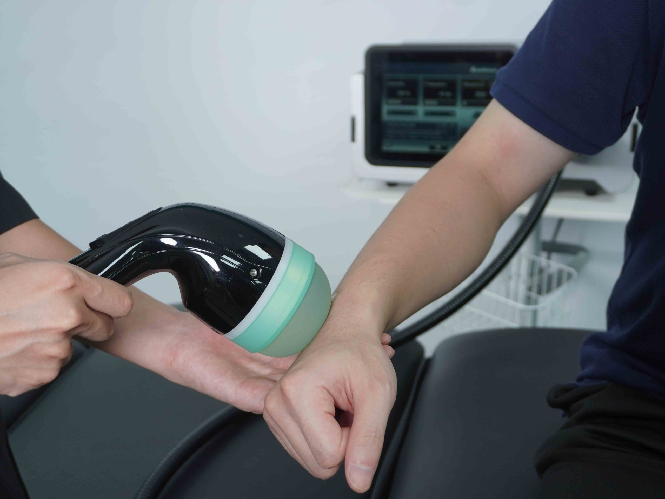 Fysioterapeut behandler arm med shockwave-apparat hos Fysio Vallensbæk
